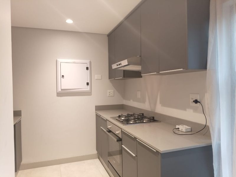 Modern kitchen featuring grey cabinetry, stone countertops, a built-in gas hob, and an integrated extractor fan.