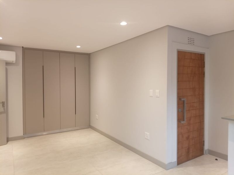 A modern, neutral-toned interior space featuring built-in floor-to-ceiling cabinetry, recessed downlighting, and a solid timber entrance door with contemporary hardware.