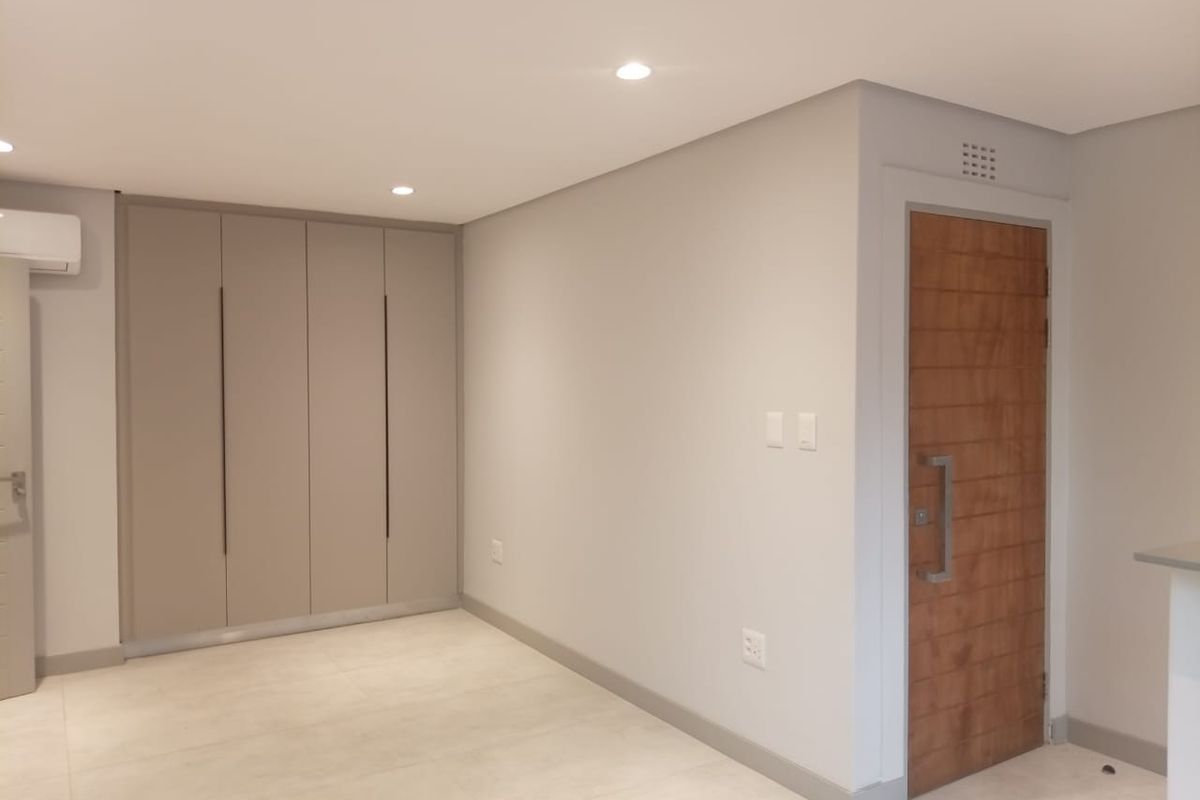 A modern, neutral-toned interior space featuring built-in floor-to-ceiling cabinetry, recessed downlighting, and a solid timber entrance door with contemporary hardware.
