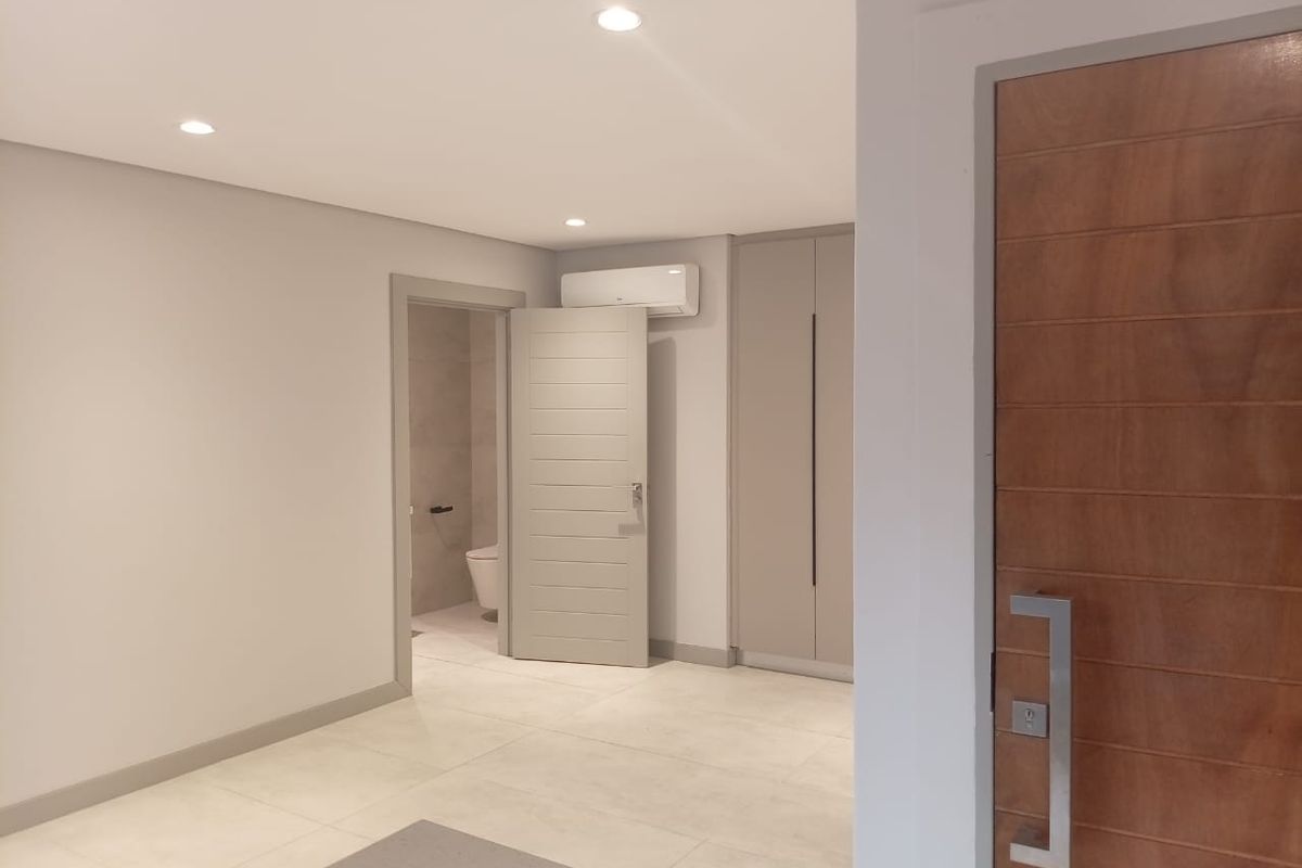 A modern bedroom featuring neutral tiled flooring, built-in cabinetry, recessed ceiling lighting, and an en-suite bathroom with a wall-mounted air conditioning unit.