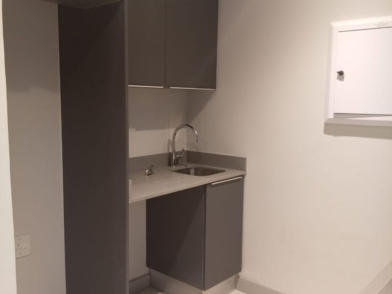 A compact, modern laundry area featuring sleek grey cabinetry, a stainless steel sink with a chrome faucet, and tiled flooring.
