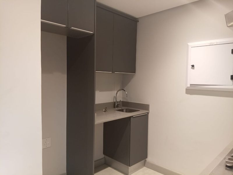 A compact, modern scullery area featuring dark grey cabinetry, a stainless steel sink with a chrome faucet, and a dedicated space for appliances.