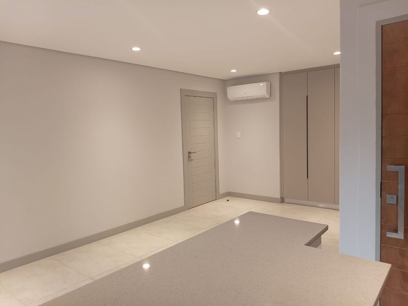 Modern interior space featuring neutral tones, tiled flooring, recessed lighting, a wall-mounted air conditioning unit, and built-in cabinetry.