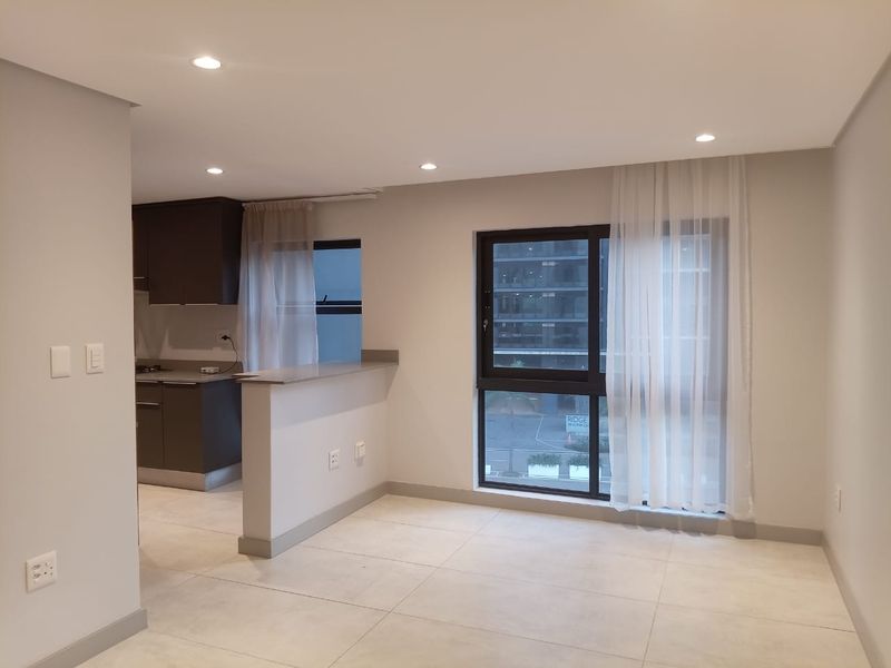An open-plan living area featuring tiled flooring, recessed lighting, and a modern kitchen with dark cabinetry and a breakfast bar.