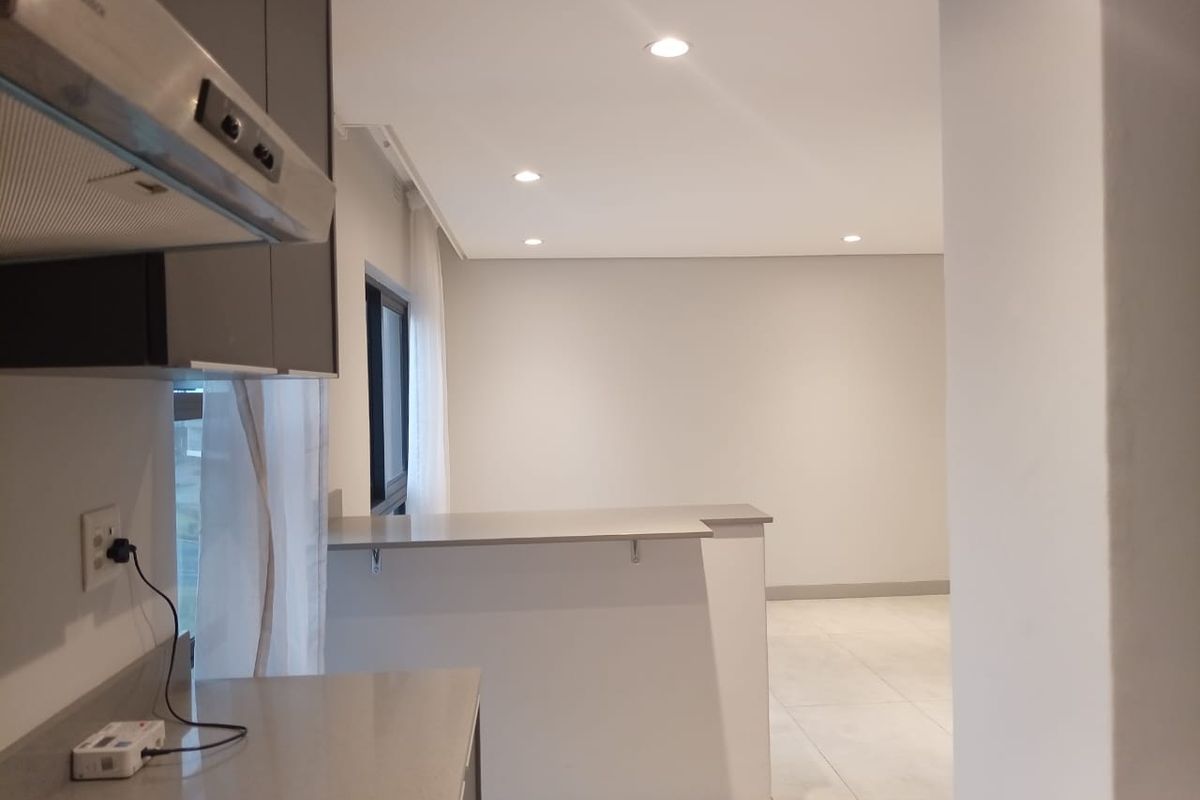 Modern open-plan kitchen and living area featuring sleek cabinetry, stone countertops, a stainless steel extractor fan, and recessed ceiling lighting.