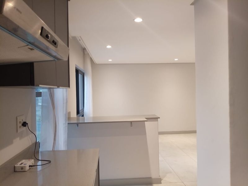 Modern open-plan kitchen and living area featuring sleek cabinetry, stone countertops, a stainless steel extractor fan, and recessed ceiling lighting.