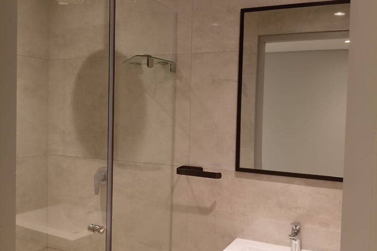 Modern bathroom featuring a glass-enclosed walk-in shower, contemporary vanity with basin, and a sleek framed mirror.