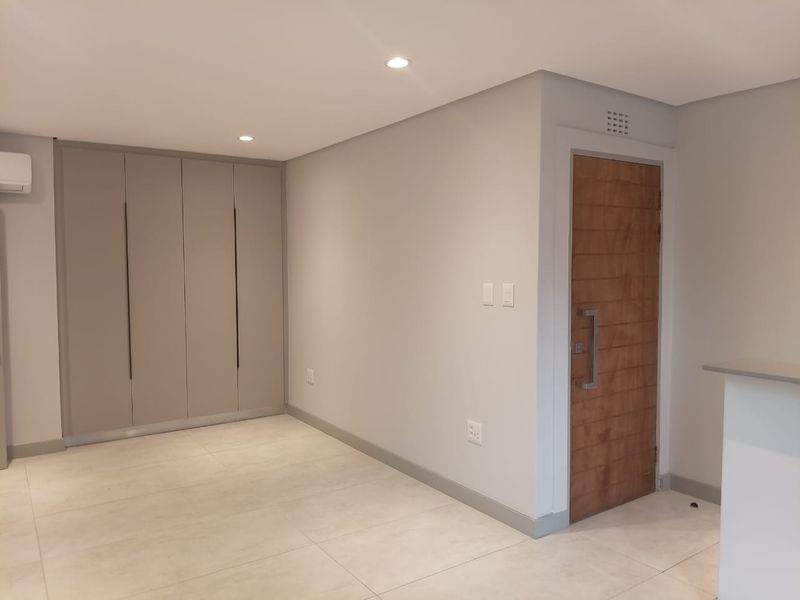 A clean, modern interior space featuring neutral tiled flooring, built-in cabinetry, and a solid wood entrance door with contemporary hardware.