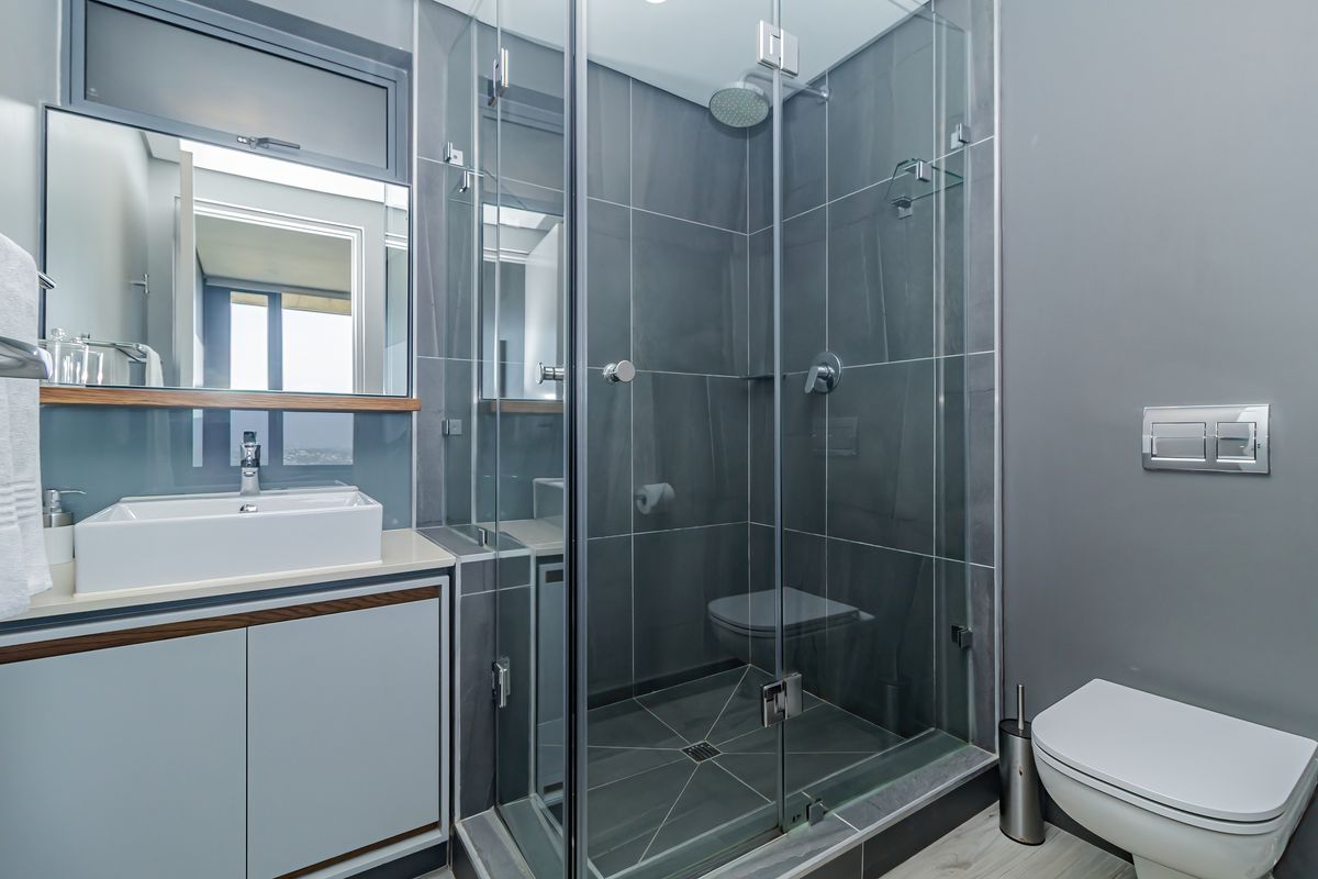 Modern bathroom featuring a glass-enclosed shower, wall-mounted toilet, vanity with vessel sink, and contemporary grey tiling.