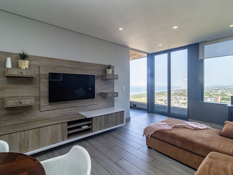 Modern living room featuring a custom built-in media unit, sleek tiled flooring, and expansive floor-to-ceiling glass doors offering panoramic coastal views.