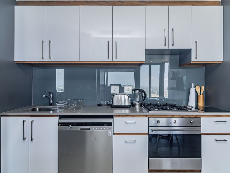 Modern kitchen featuring sleek white cabinetry, stone countertops, a glass splashback, and high-quality integrated stainless steel appliances.