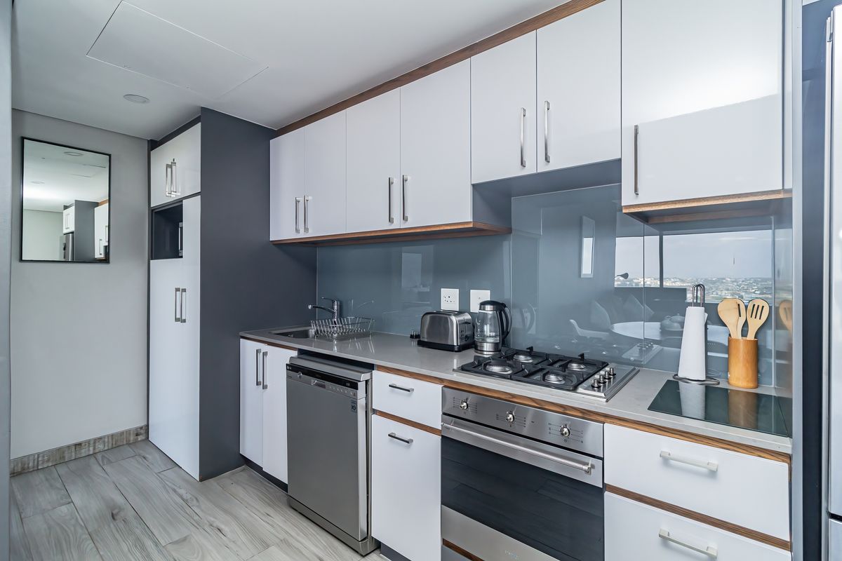 Modern kitchen featuring sleek white cabinetry, stone countertops, a gas hob, built-in oven, and high-quality glass splashback with integrated appliances.