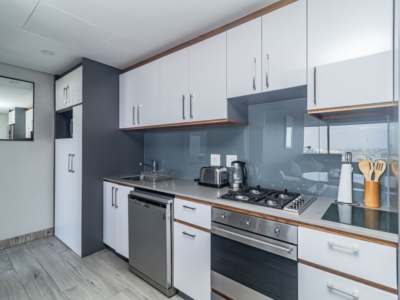 Modern kitchen featuring sleek white cabinetry, stone countertops, a gas hob, built-in oven, and high-quality glass splashback with integrated appliances.