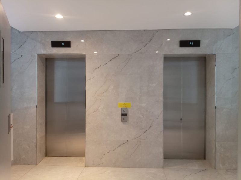 Modern apartment building elevator lobby featuring dual stainless steel elevator doors and elegant marble-look wall tiling.