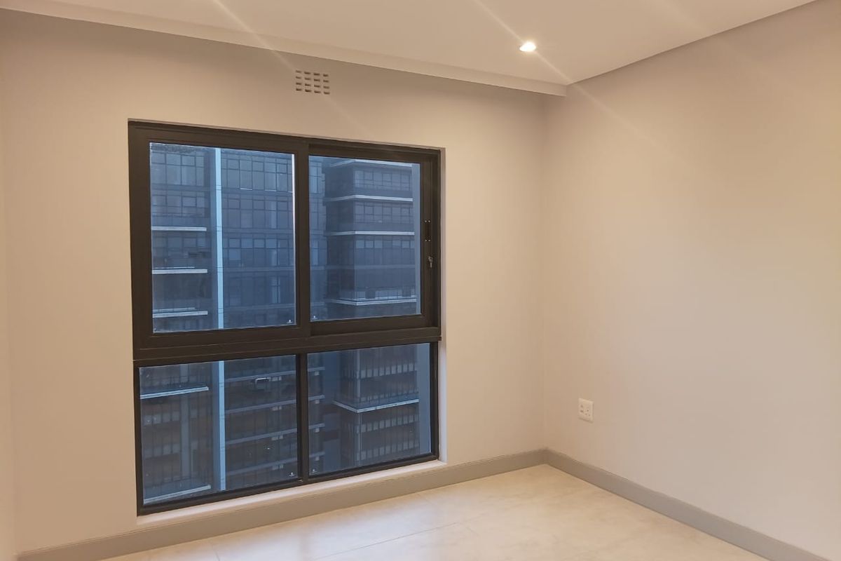 A bright, empty bedroom featuring modern tiled flooring, neutral walls, recessed ceiling lighting, and a large window with dark frames.