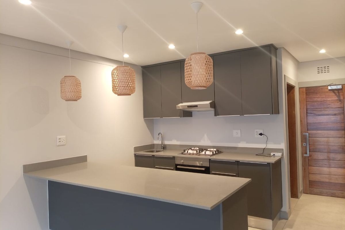 Modern kitchen featuring sleek grey cabinetry, stone countertops, a built-in gas hob, extractor fan, and a breakfast bar island.