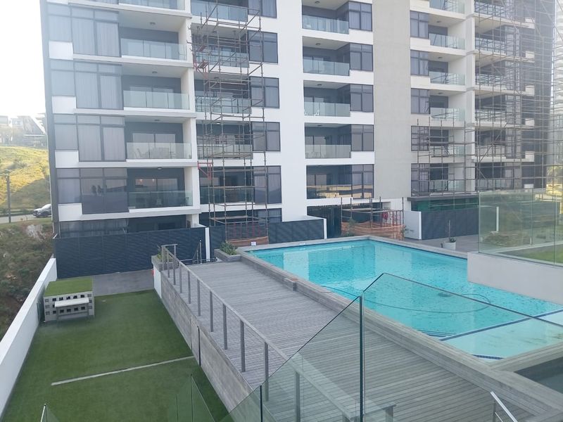 View of the apartment complex exterior featuring a swimming pool, timber decking, and landscaped garden area.