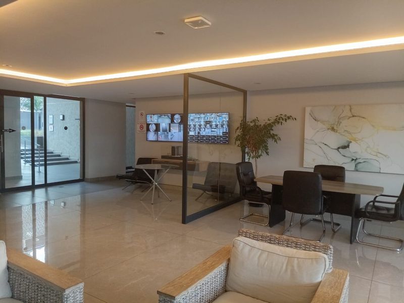 Modern apartment building lobby featuring polished tile flooring, recessed ceiling lighting, and a glass-partitioned office or meeting area.