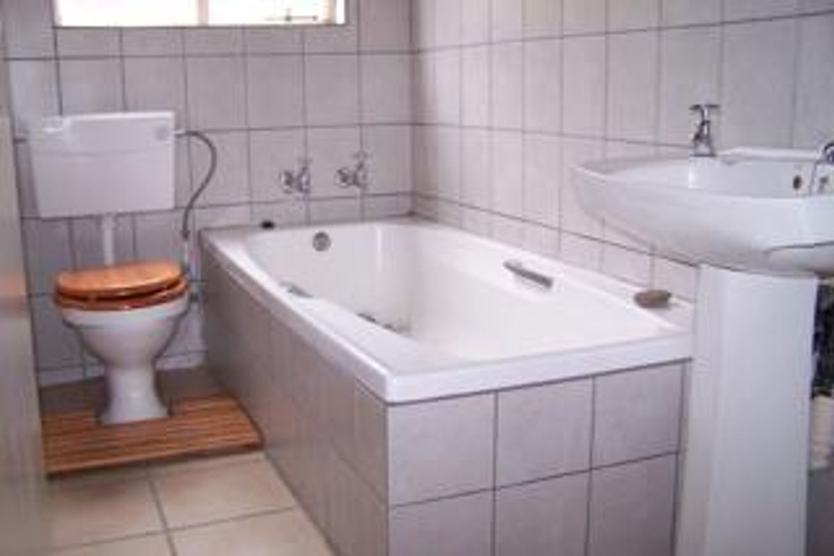 A functional bathroom featuring a standard bathtub, pedestal basin, and toilet with full-height wall tiling.