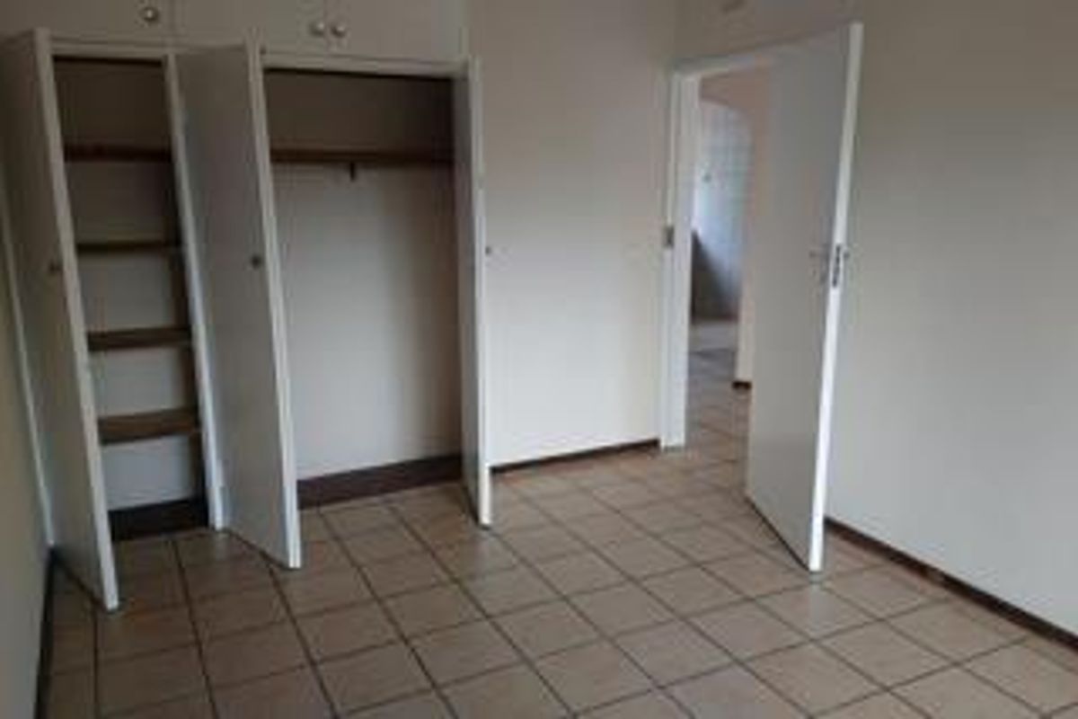 An empty bedroom featuring built-in storage cupboards, tiled flooring, and a doorway leading to an adjacent room.