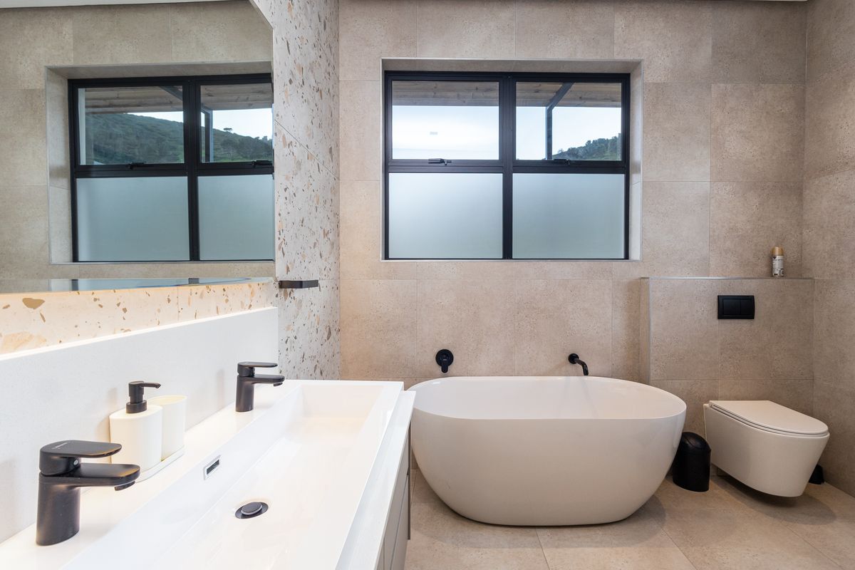 Modern bathroom featuring a sleek freestanding bathtub, wall-hung toilet with concealed cistern, double vanity basin, and contemporary matte black fixtures with terrazzo tiling.