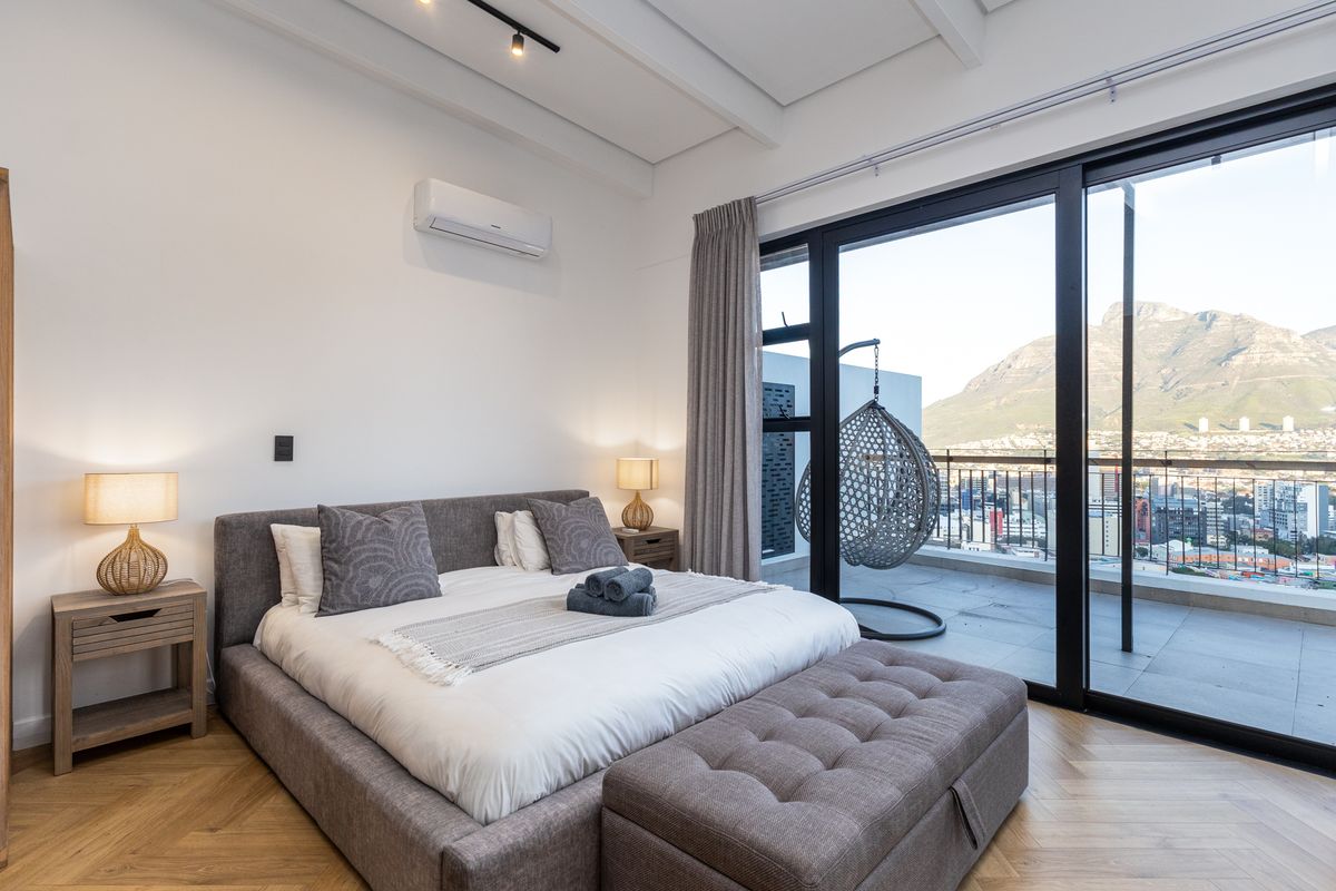 Modern bedroom featuring herringbone timber flooring, exposed beam ceiling, and large sliding glass doors opening to a balcony with mountain and city views.