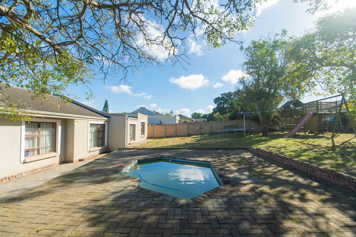 Rear garden featuring a paved patio area, a small swimming pool, and a spacious lawn with established trees and perimeter fencing.