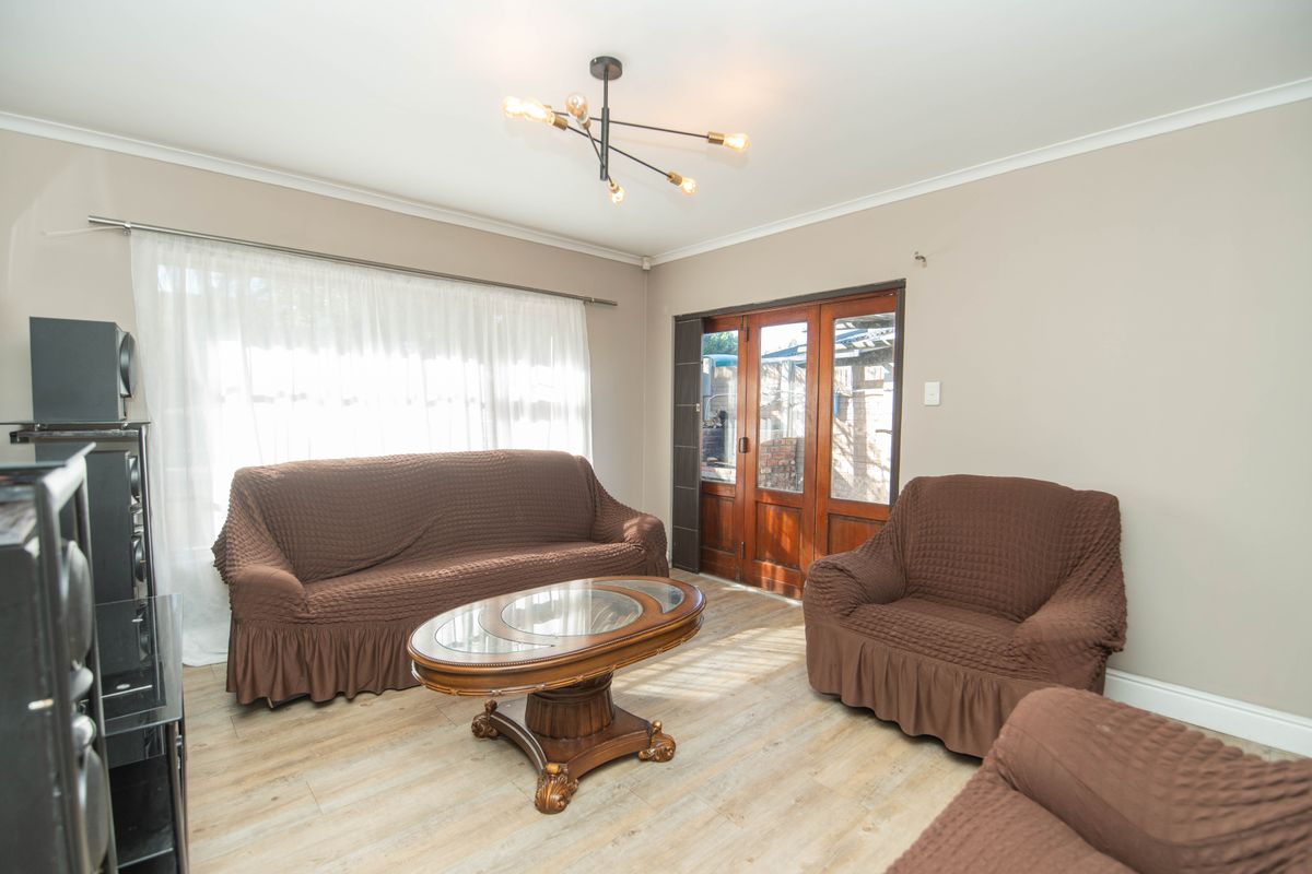 A living room featuring light wood-look flooring, a modern multi-arm ceiling light fixture, and timber-framed glass doors leading to the exterior.