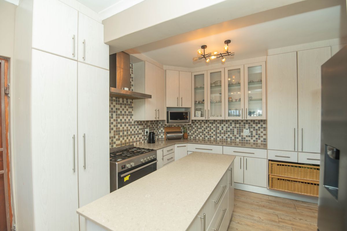 Modern kitchen featuring light wood cabinetry, stone countertops, a central island, mosaic tile backsplash, and built-in stainless steel appliances.
