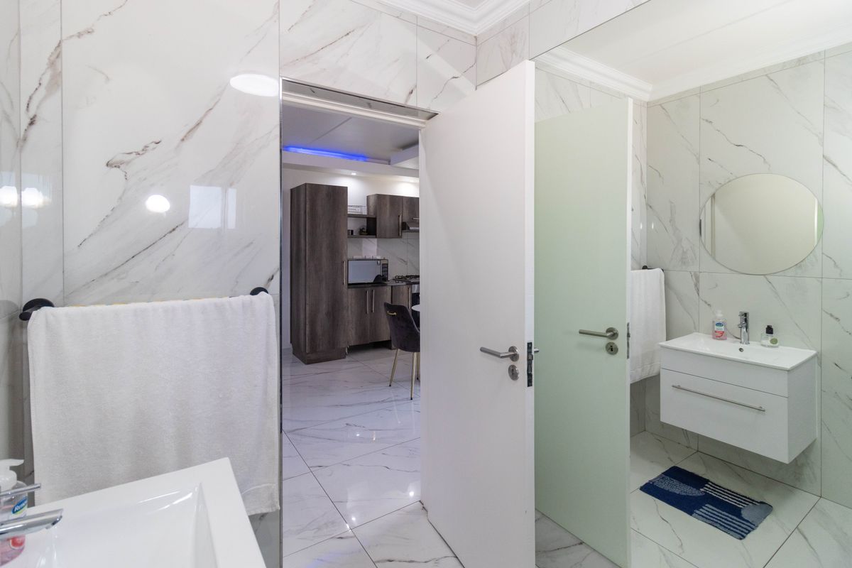 Modern bathroom featuring marble-look wall tiles, a floating vanity with integrated basin, and a circular mirror, with a view into the adjacent kitchen area.
