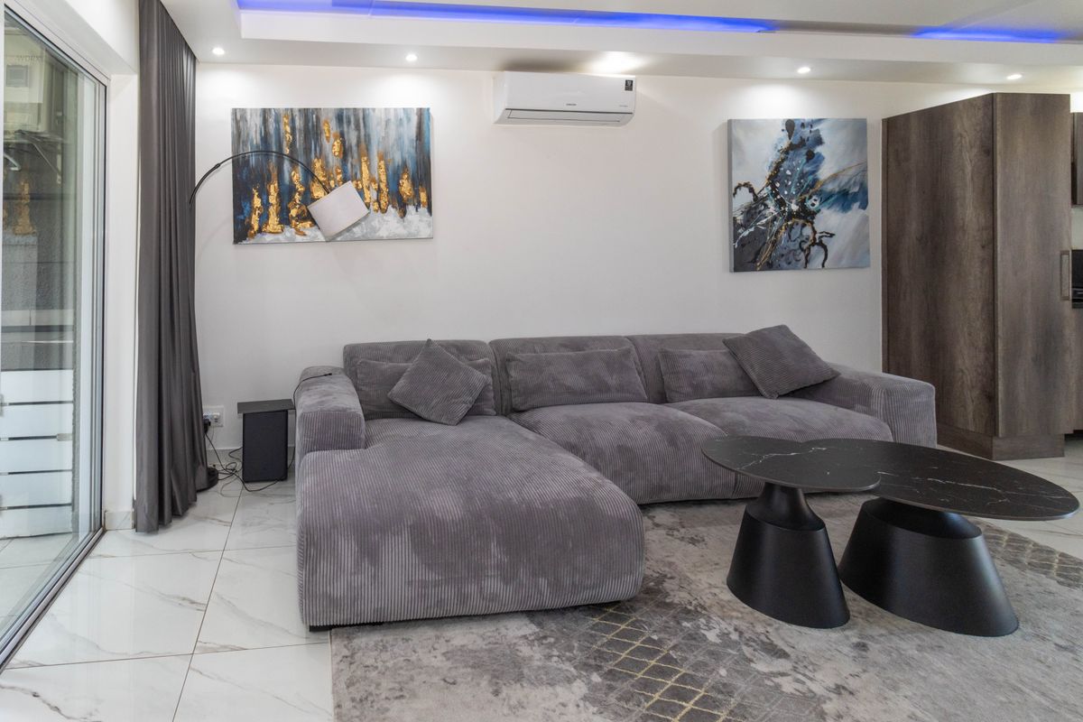 Modern living area featuring polished marble-look floor tiles, recessed ceiling lighting with blue accent strip, and a wall-mounted air conditioning unit.