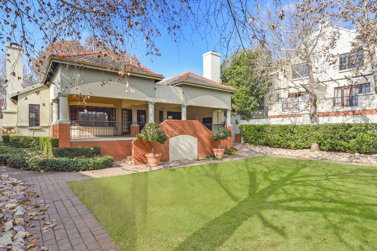 A well-maintained rear exterior view featuring a covered patio, brick staircase, landscaped lawn, and established garden beds.