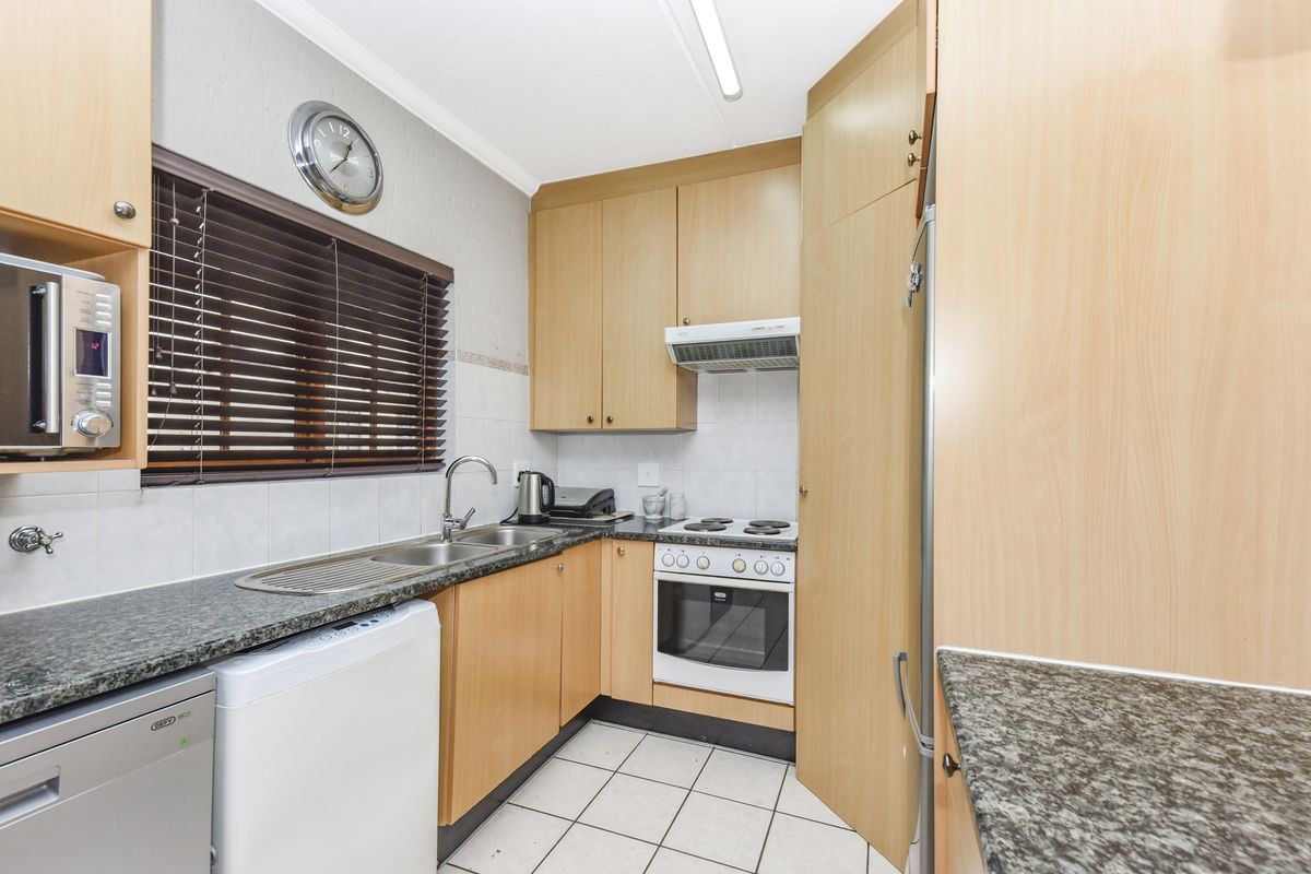 Functional kitchen featuring light wood cabinetry, granite-look countertops, tiled flooring, and a built-in oven with extractor fan.