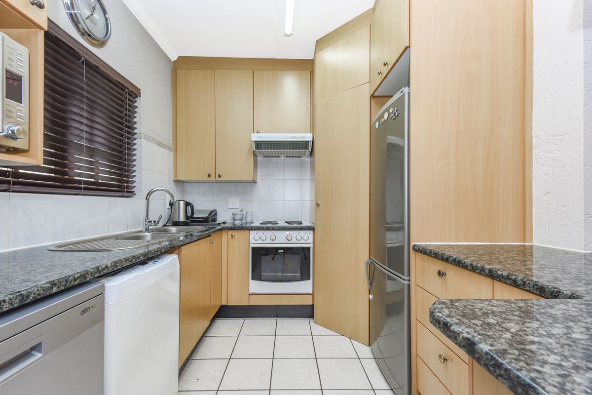 A functional galley-style kitchen featuring light wood cabinetry, granite countertops, tiled backsplash, and built-in oven with extractor fan.