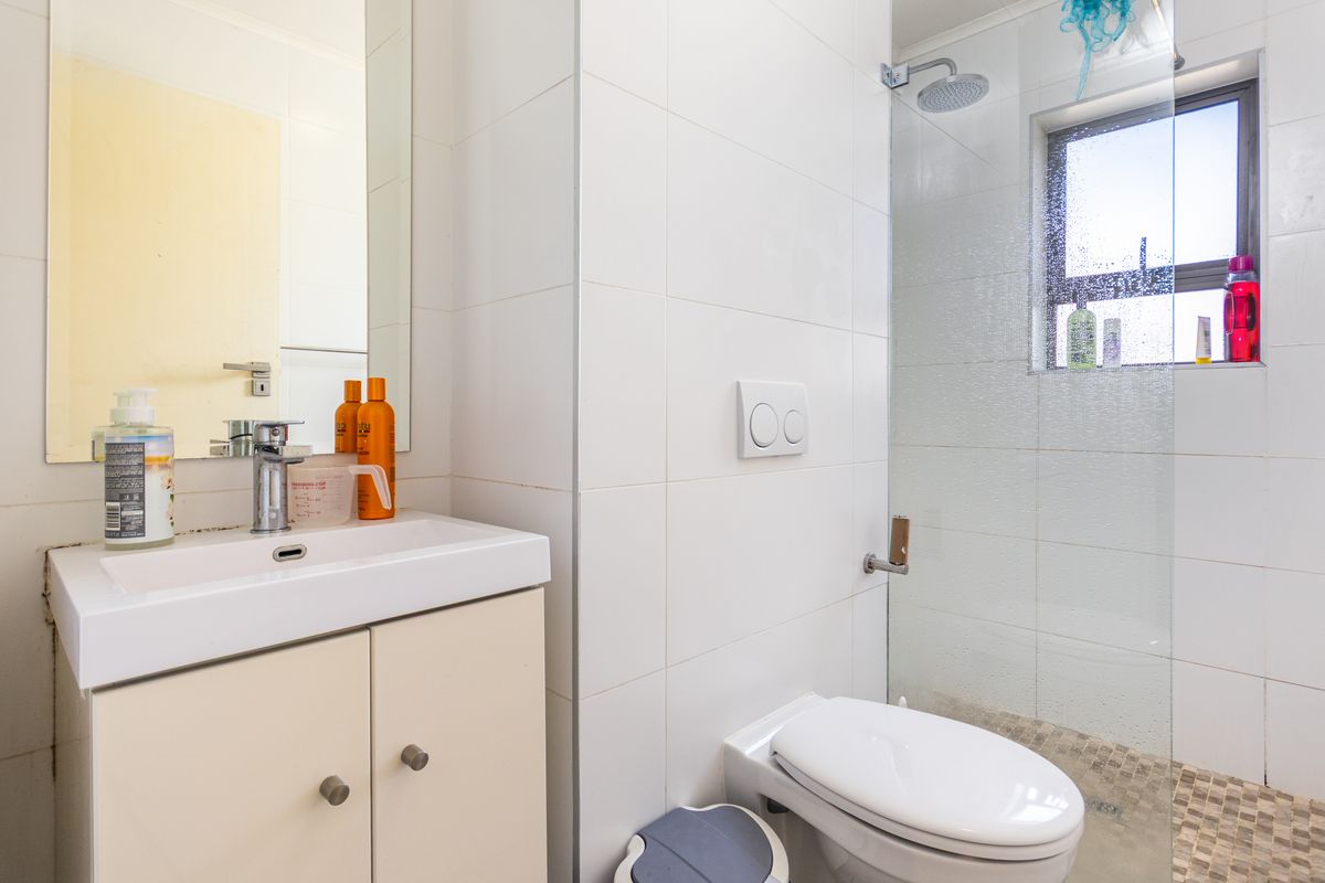 A compact bathroom featuring a wall-mounted toilet, a glass-enclosed shower with a rainfall showerhead, and a vanity basin with a mirror.