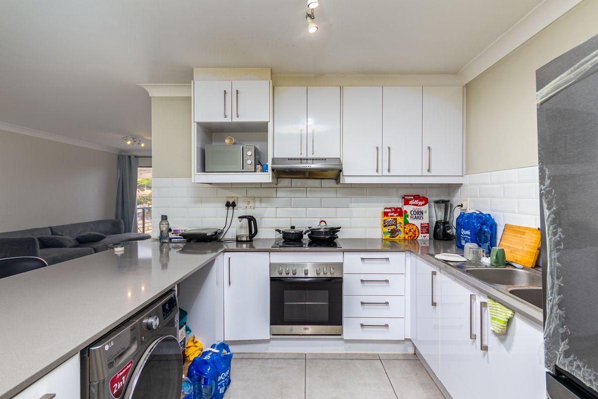 Modern kitchen featuring white cabinetry, stone countertops, subway tile backsplash, built-in oven, extractor fan, and integrated laundry appliance space.
