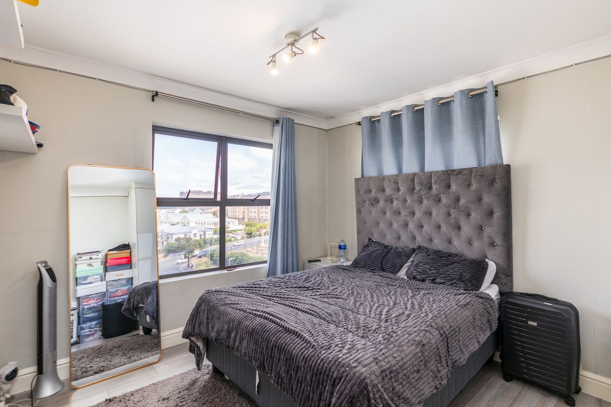 A well-lit bedroom featuring large windows with urban views, neutral wall finishes, and modern ceiling-mounted track lighting.