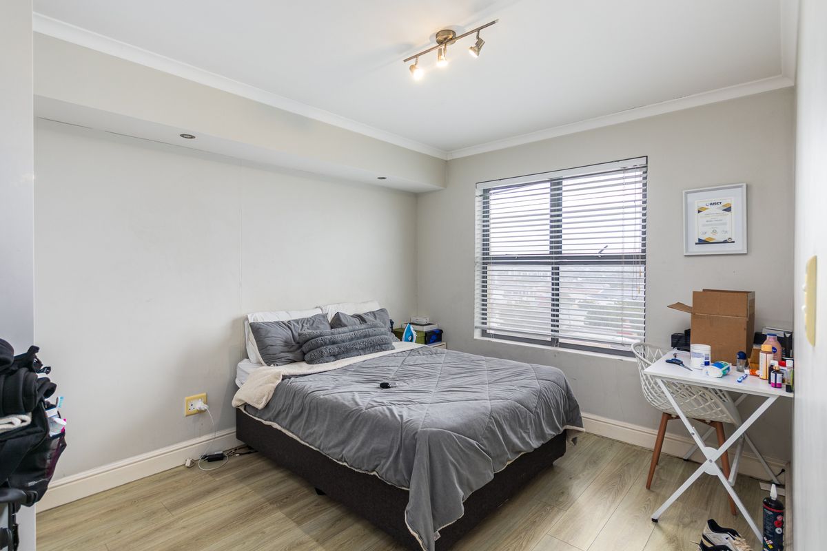 A well-lit bedroom featuring light wood-look flooring, a large window with fitted blinds, and modern ceiling-mounted spotlight fixtures.