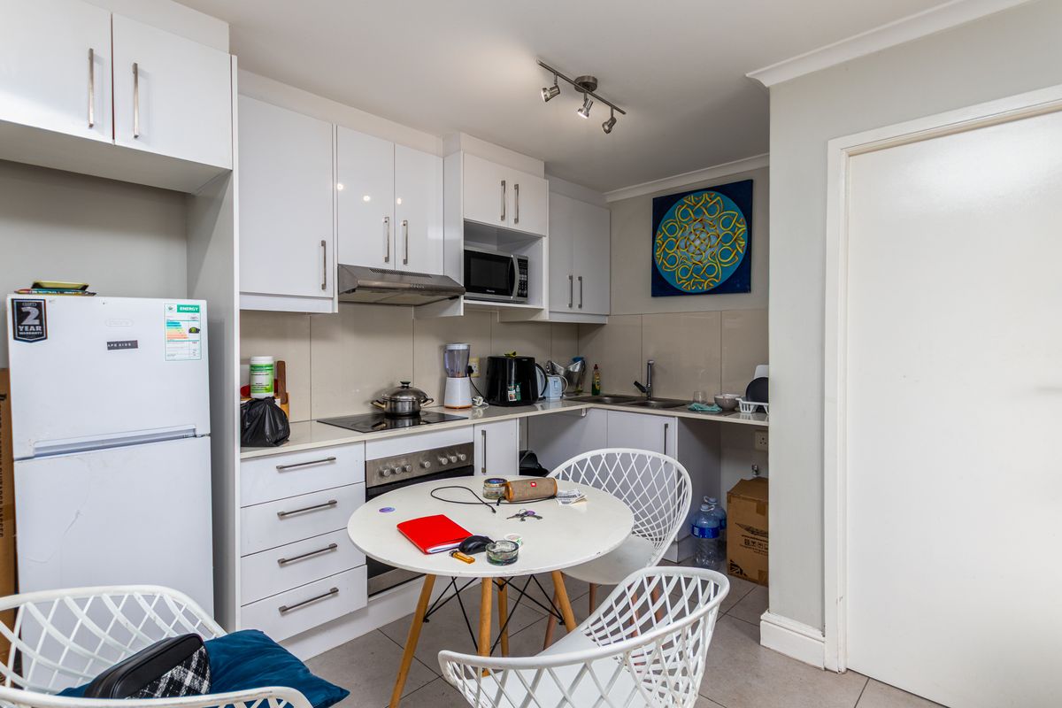 Compact kitchen featuring white cabinetry, integrated oven, hob, extractor fan, and built-in microwave with tiled splashbacks and tiled flooring.