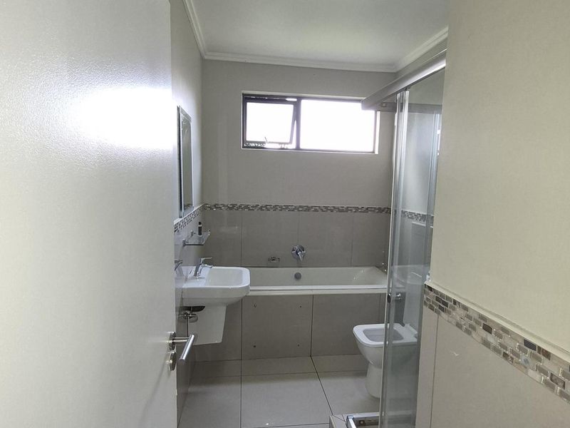 A functional bathroom featuring a bathtub, separate glass-enclosed shower, wall-mounted basin, and tiled flooring with neutral wall finishes.