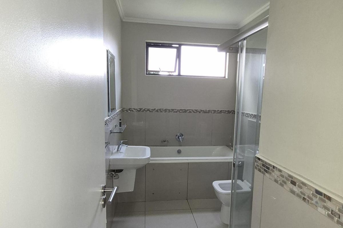 A functional bathroom featuring a bathtub, separate glass-enclosed shower, wall-mounted basin, and tiled flooring with neutral wall finishes.
