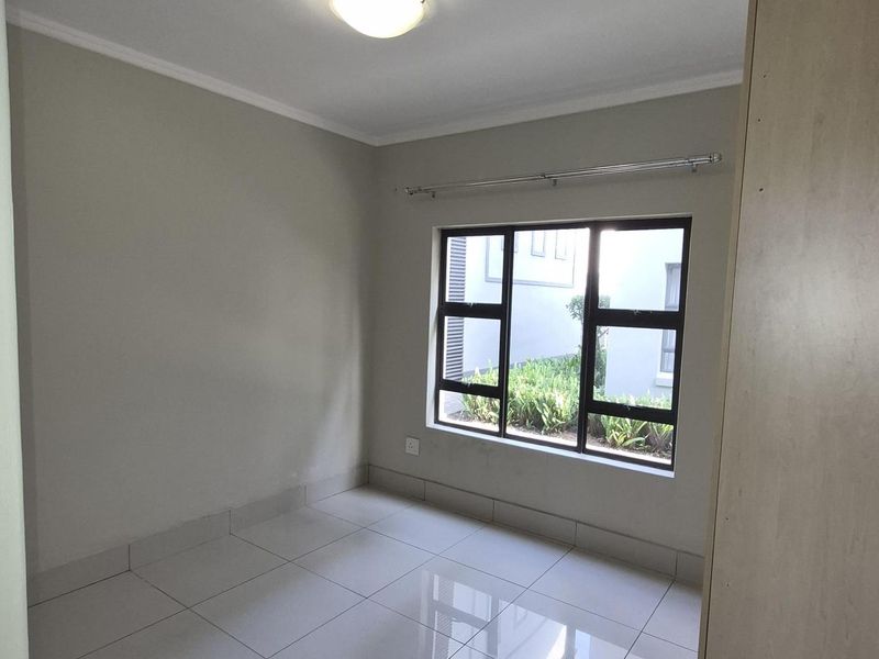 A bright, empty bedroom featuring neutral tiled flooring, a built-in cupboard, and a large window providing natural light.