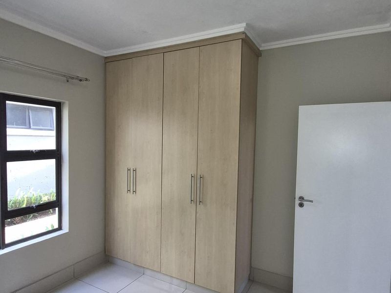 A bright bedroom featuring neutral tiled flooring, built-in wooden cabinetry, and a window providing natural light.