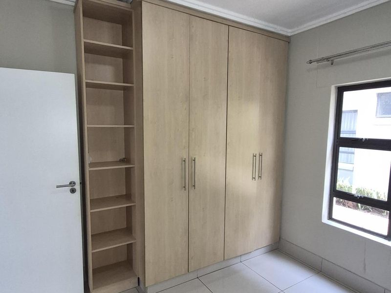 A bedroom featuring built-in light wood cabinetry with integrated shelving, tiled flooring, and a window with a curtain rod.