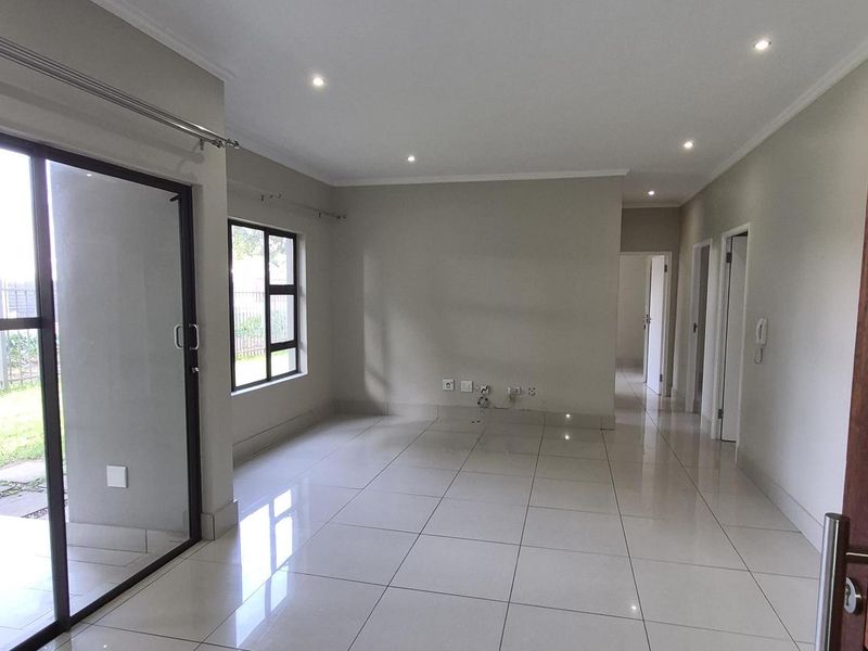 A bright, open-plan living area featuring neutral tiled flooring, recessed downlighting, and large sliding glass doors providing access to the outdoor space.