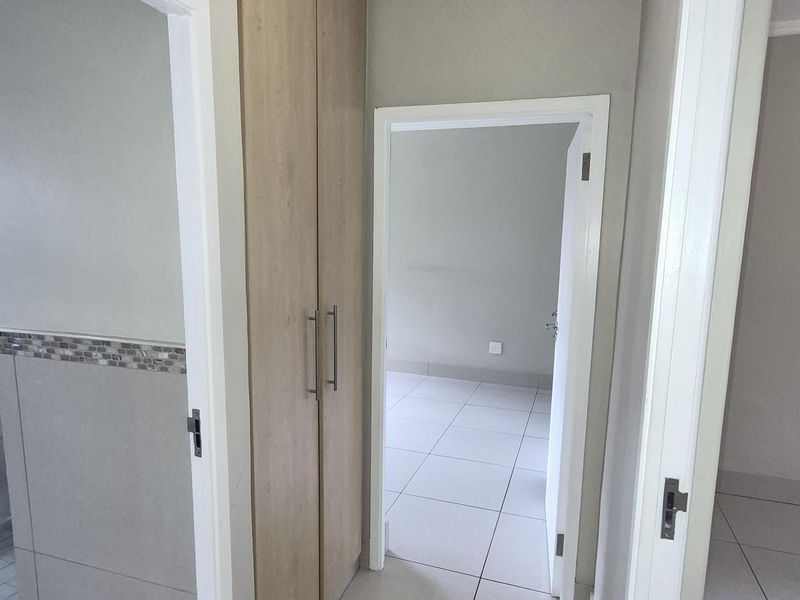 A clean hallway featuring light-toned floor tiles and a built-in wooden cupboard, providing access to adjacent rooms.