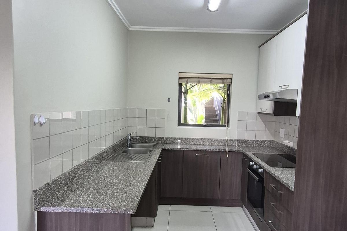 A functional kitchen featuring dark wood cabinetry, granite countertops, a built-in oven, hob, extractor fan, and tiled flooring.