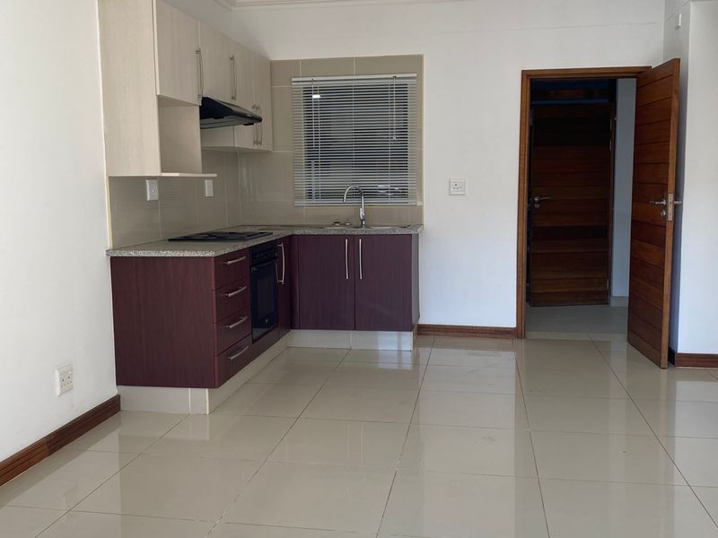 Open plan kitchen featuring two-tone cabinetry, built-in oven, hob, extractor fan, and tiled flooring, seamlessly integrated into the living area.