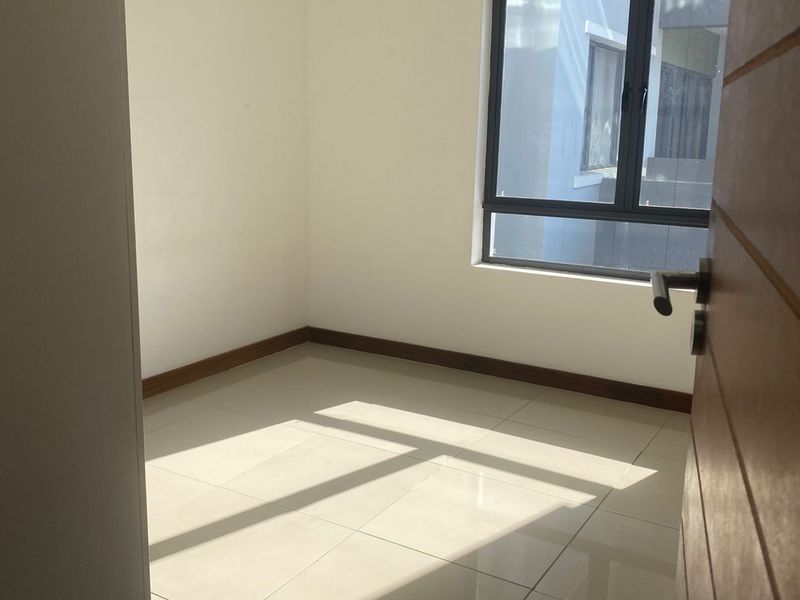 A bright, empty bedroom featuring neutral tiled flooring, clean white walls, and a modern dark-framed window.