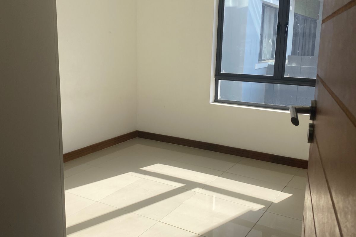 A bright, empty bedroom featuring neutral tiled flooring, clean white walls, and a modern dark-framed window.